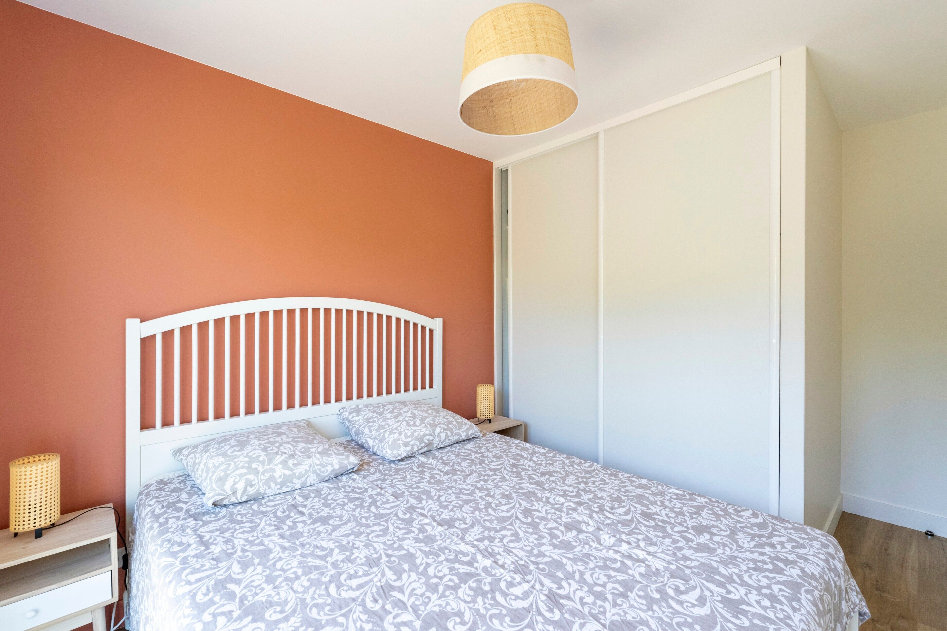 Een slaapkamer met een wit bed, nachtkastje, lamp en een kledingkast.