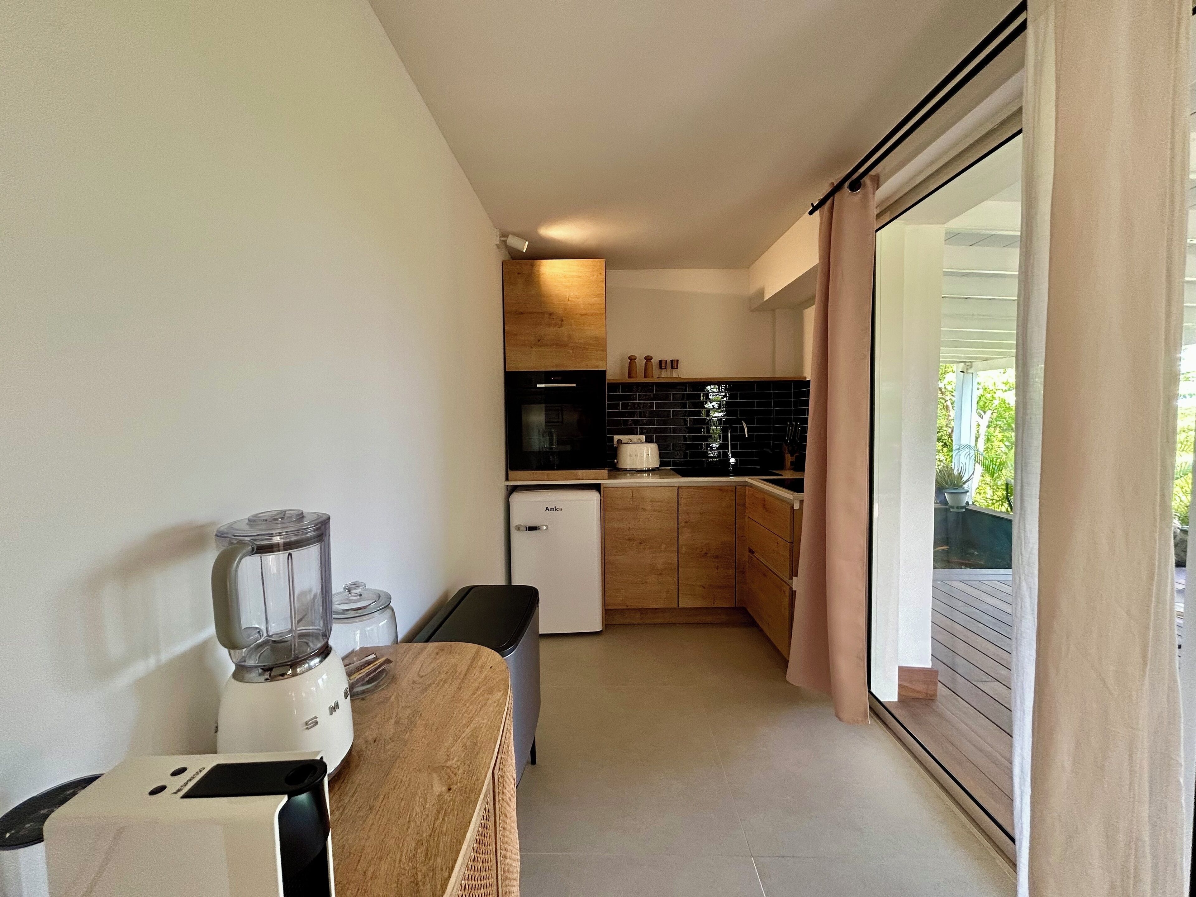 A compact kitchen with a blender, a small refrigerator, and wooden cabinets.