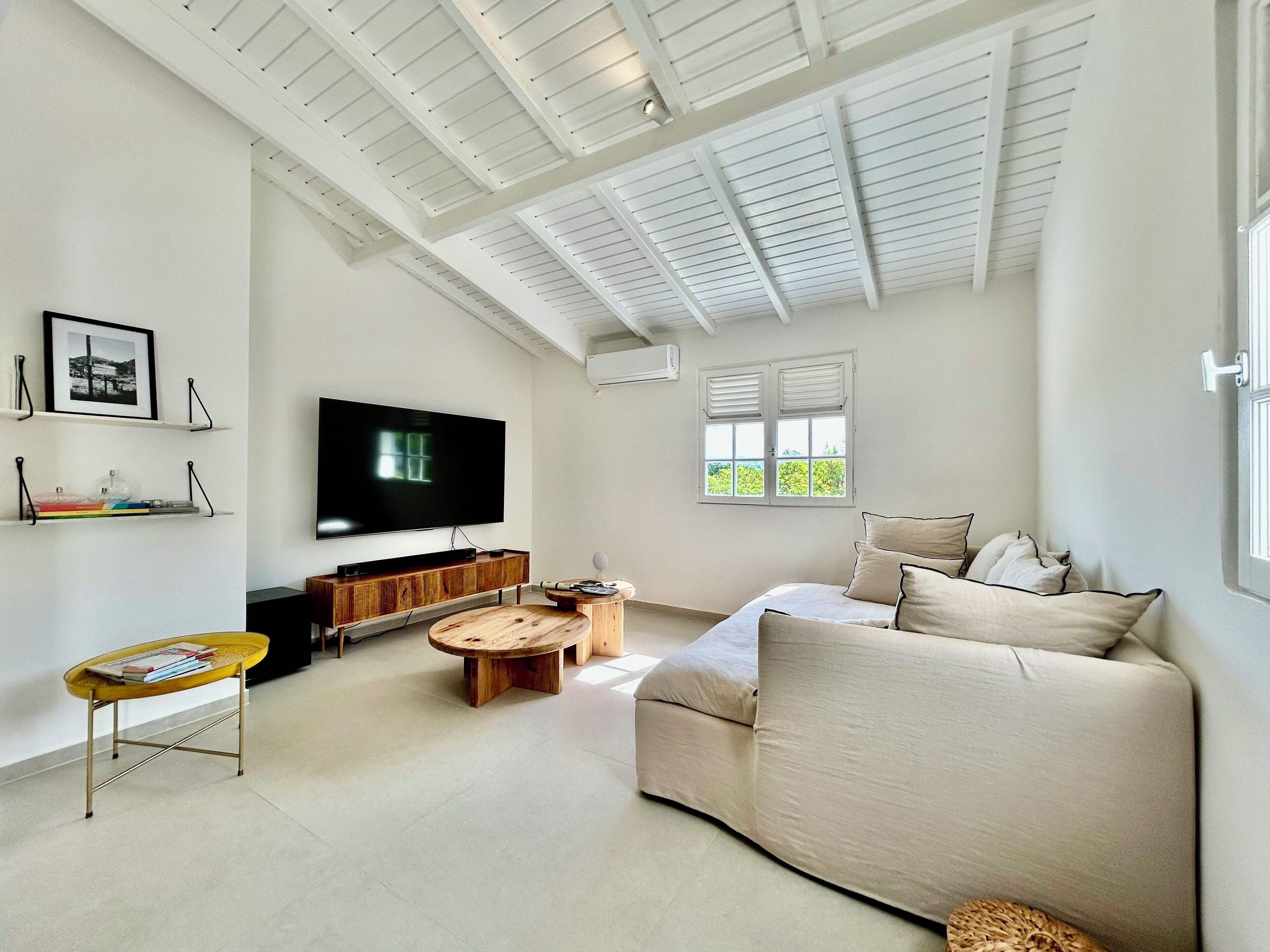 A spacious living room with a large flat-screen TV, a sofa, a coffee table, and a bookshelf.
