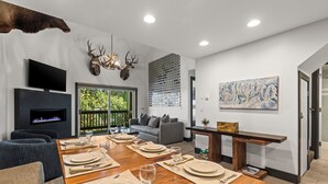 A modern living room with a fireplace, a dining area set for six, and a mounted deer head on the wall.