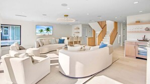 A modern living room with a curved white sofa, a dining area, and a kitchen with wooden cabinets. - Siesta Beachfront Paradise - Infinity Pool & Spa! (Sarasota)