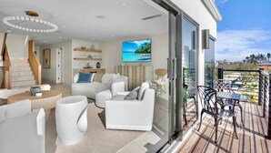 A modern living room with a large TV, white furniture, and a balcony with outdoor seating. - Siesta Beachfront Paradise - Infinity Pool & Spa! (Sarasota)