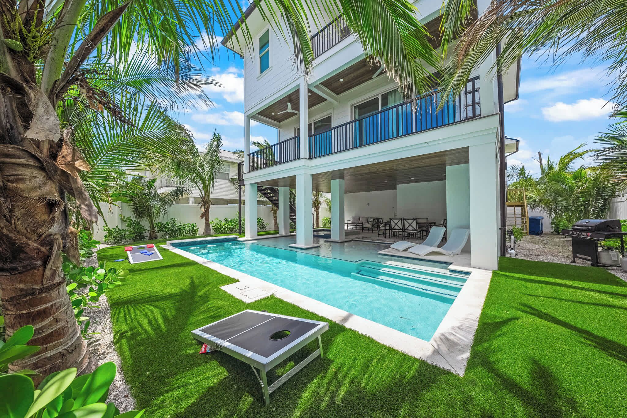 Ein zweistöckiges Haus mit Swimmingpool, Sitzgelegenheit im Freien und Palmen.
