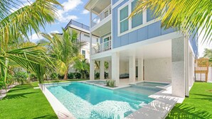 A two-story house with a swimming pool, surrounded by palm trees and a well-maintained lawn. - Beach View Paradise - New Anna Maria Island Home (Bradenton Beach)