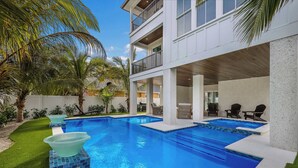 A modern two-story building with a swimming pool, outdoor seating, and palm trees.