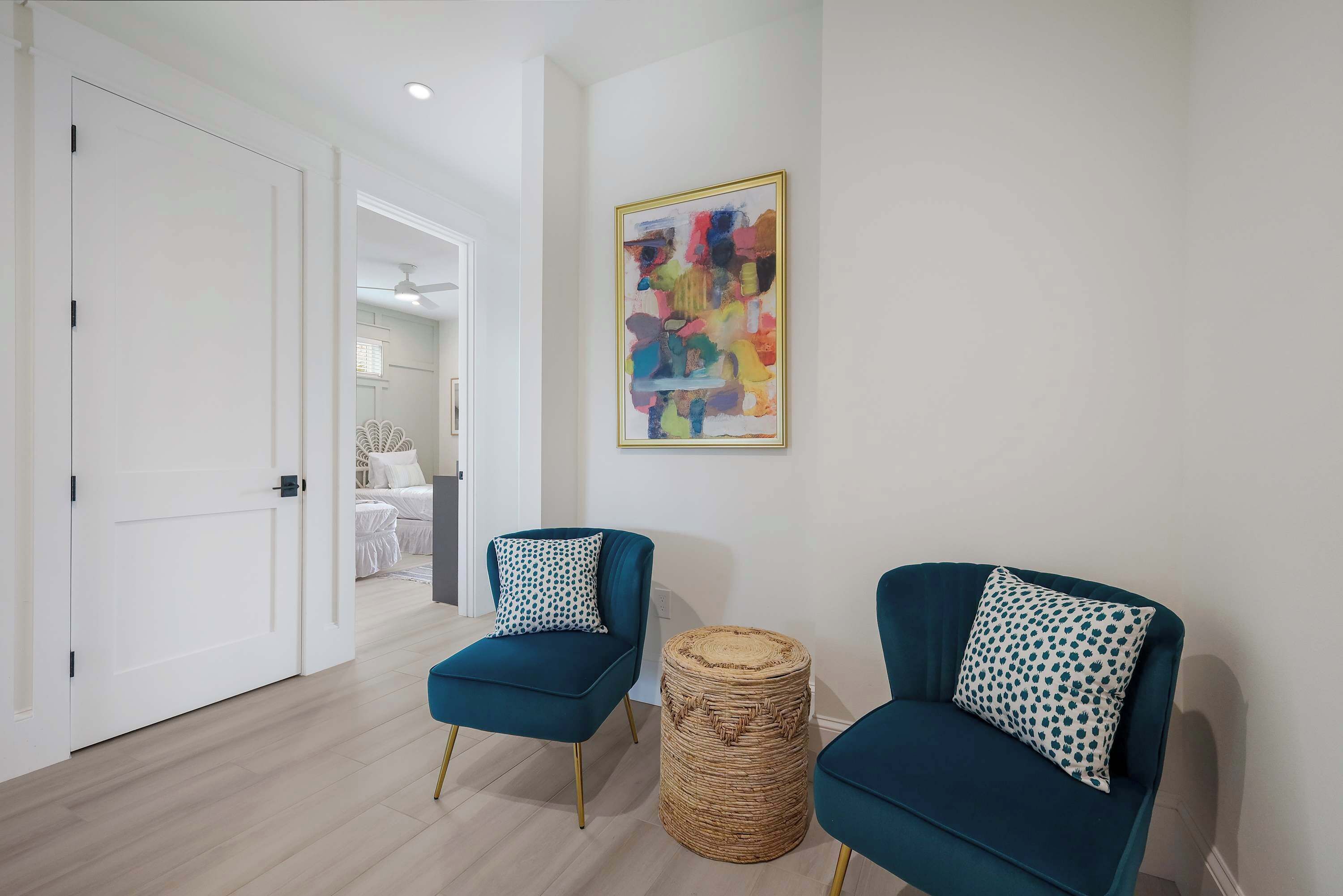 Un salon moderne avec deux fauteuils turquoise, un pouf en fibres tressées et un tableau abstrait aux couleurs vives accroché au mur.