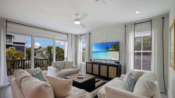 A spacious living room with a large TV, comfortable seating, and a balcony with a view of the ocean.