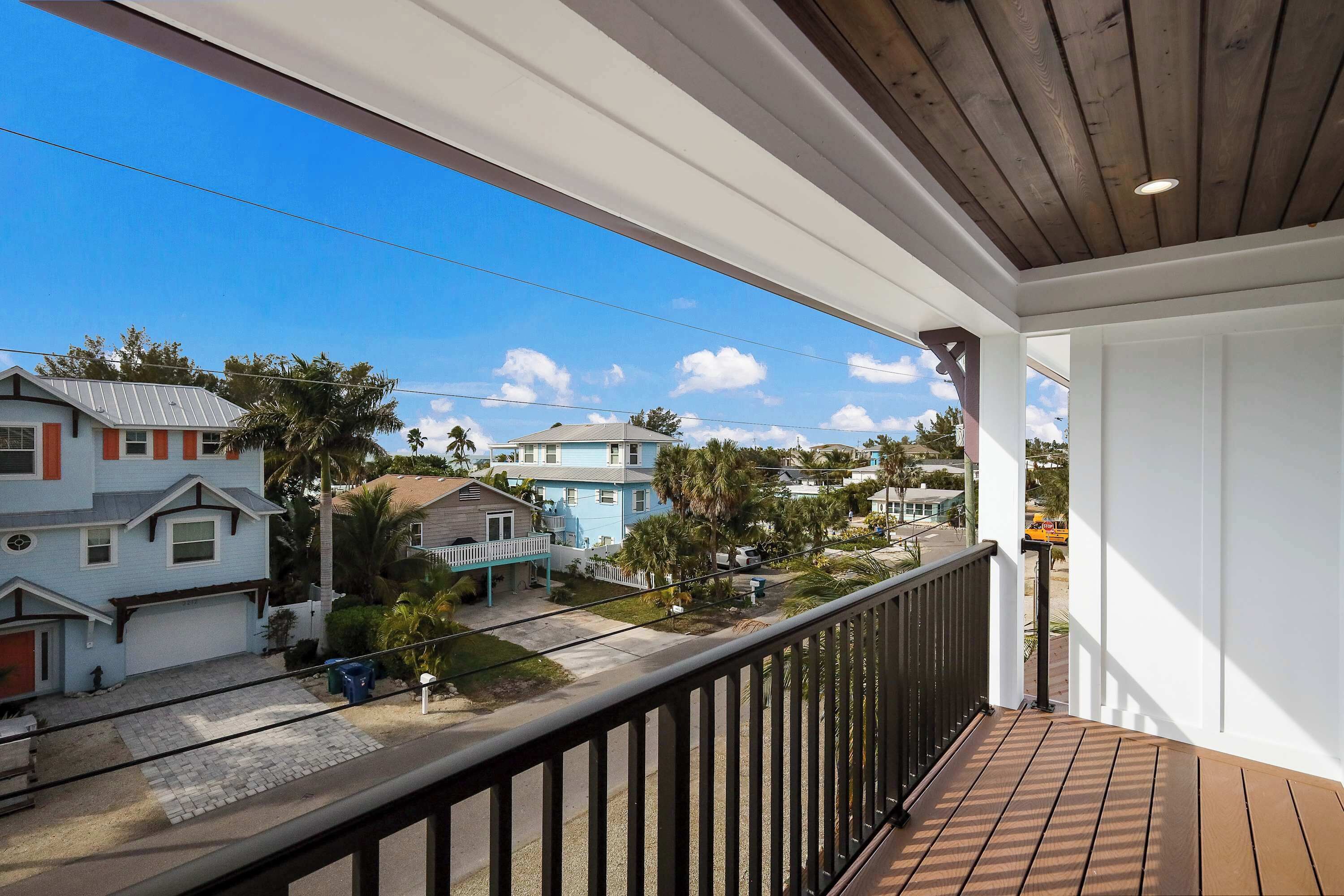 A balcony with a wooden floor and railing, overlooking a residential area with houses and palm trees.