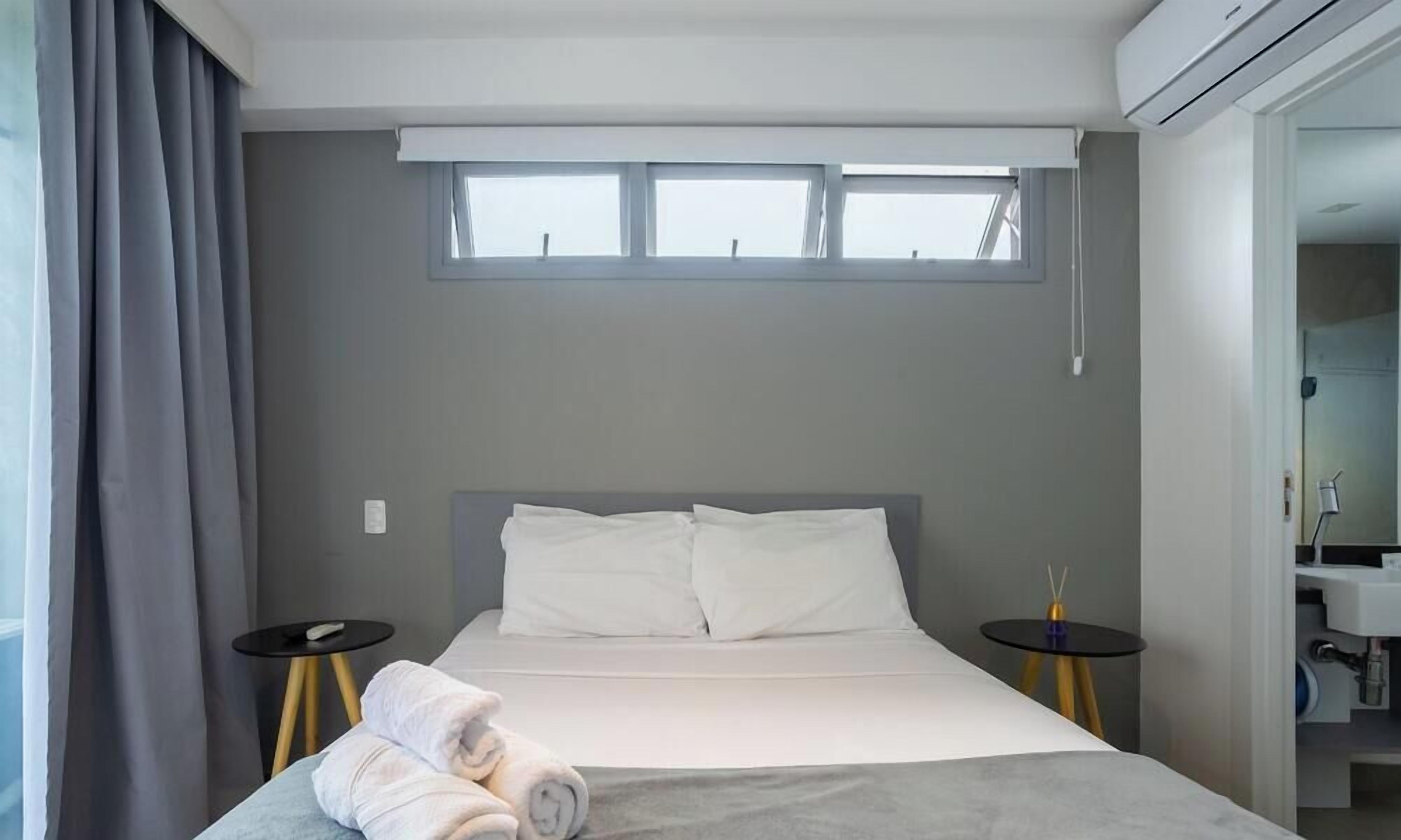 Moderni hotellihuone, jossa on sänky, kaksi yöpöytää, ikkuna ja kylpyhuone, joka näkyy avonaisen oven läpi.