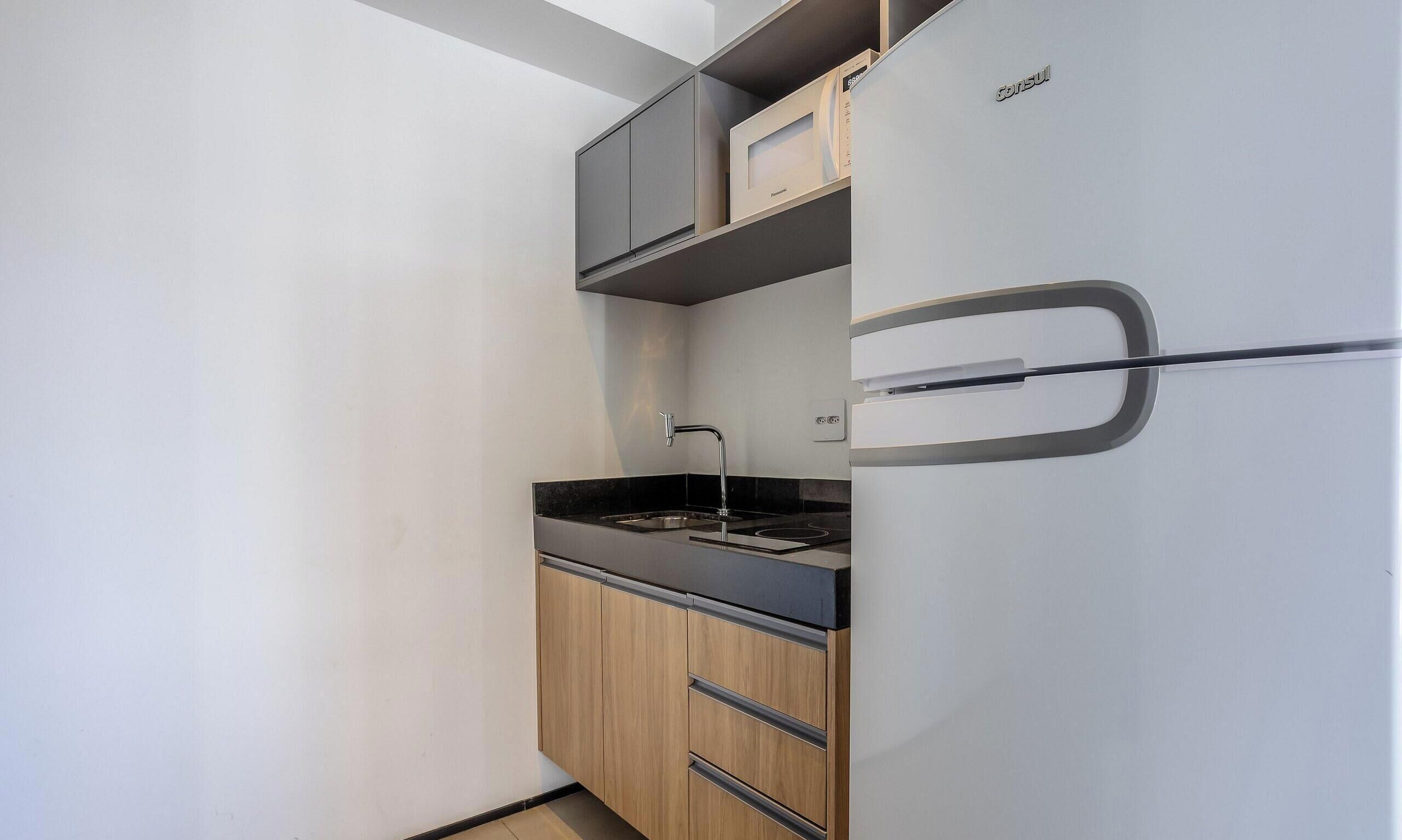 A compact kitchenette with a built-in refrigerator, a stove, and wooden cabinets.