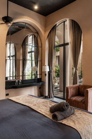 A hotel room with a large bed, a sitting area with a chair, a mirror, and a view of the outdoors.