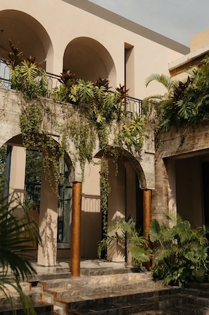 A building with a covered outdoor area featuring a staircase, columns, and lush greenery.