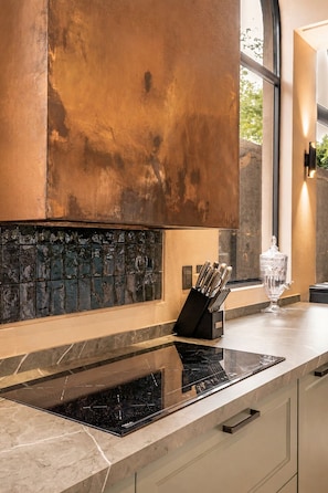 Una cocina con una placa de inducción negra, un bloque de cuchillos y un recipiente de vidrio sobre la encimera.