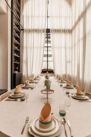 A dining table set for a meal with a view of a building through sheer curtains.