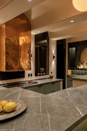A modern kitchen with a marble countertop, a large island, and a unique copper-colored wall.