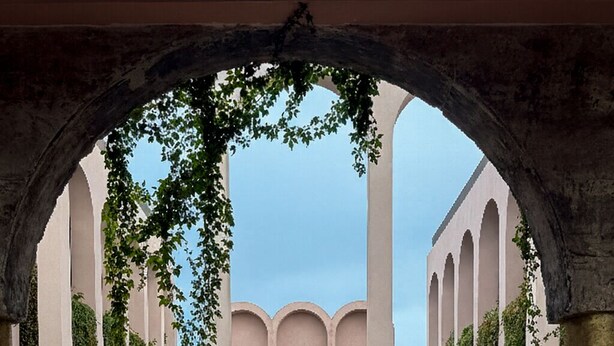 An outdoor pool area with a central water feature, surrounded by columns and greenery.