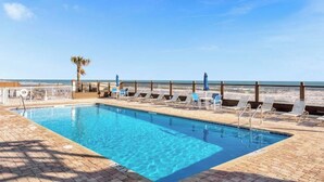 A pool with clear blue water, surrounded by lounge chairs and umbrellas, with a beach and ocean in the background. - Cozy Ocean Front Getaway ~ Sleeps 2 ~ Pools Open! (Daytona Beach)
