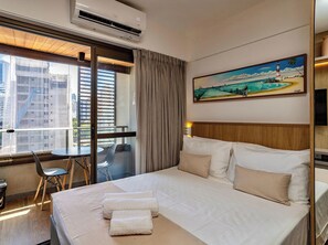 A hotel room with a bed, a desk, a chair, and a painting on the wall.