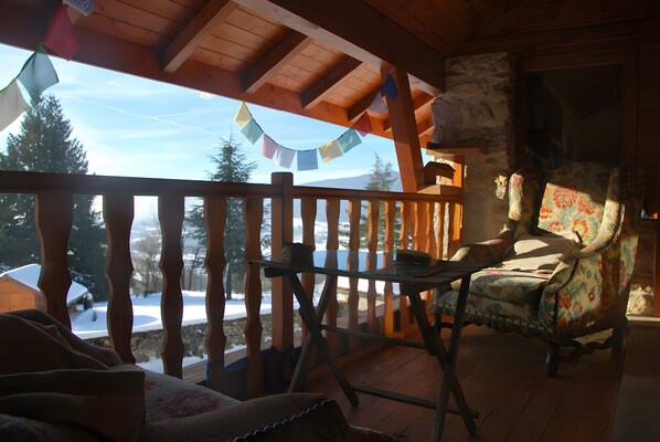 A wooden deck with a view of snow-covered ground, a rustic chair, and a table.