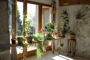 A room with large windows, a wooden table with potted plants, and a stone wall.