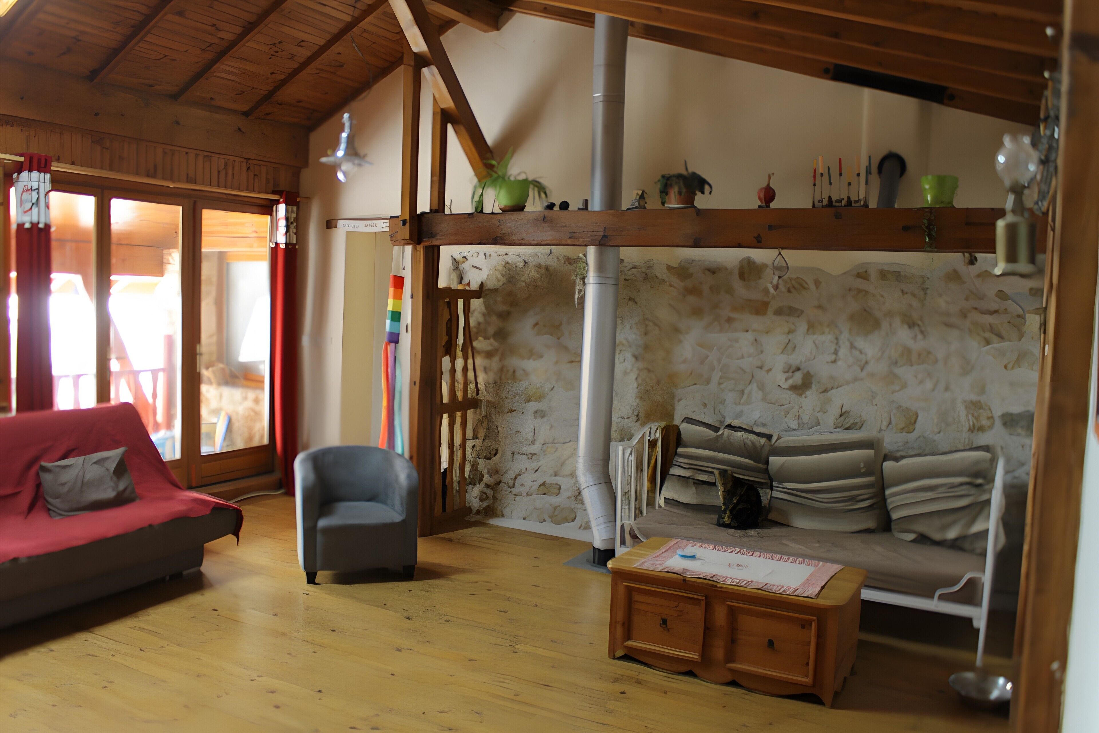 Een gezellige woonkamer met houten plafond, stenen muur, een bank, een fauteuil en een kleine tafel met papieren.