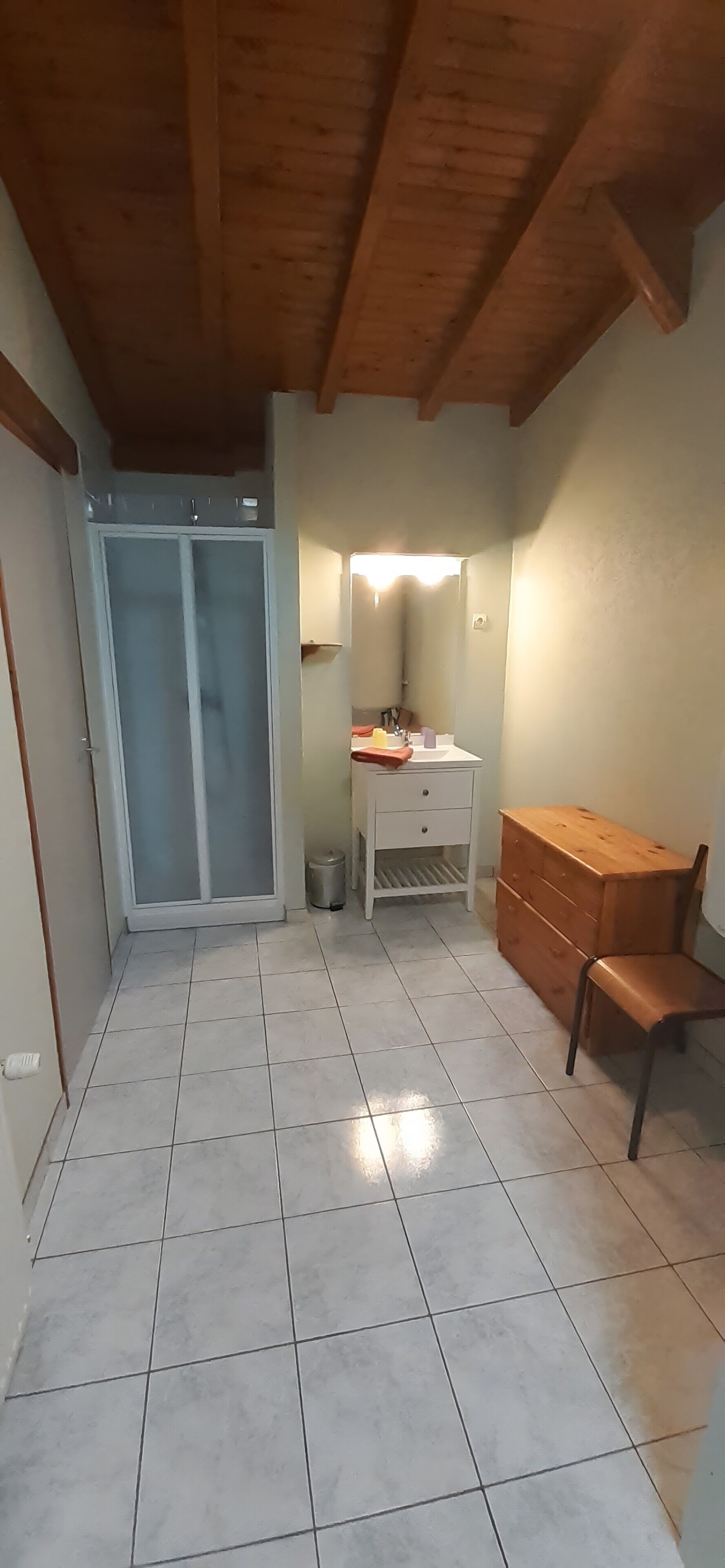 A room with a tiled floor, a wooden ceiling, a sliding glass door, a white dresser, a wooden cabinet, and a chair.