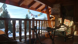 A wooden deck with a view of snow-covered ground, a rustic chair, and a table.