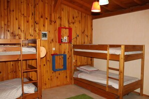 A room with wooden walls, bunk beds, a red-framed mirror, and a green rug.