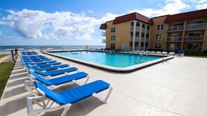A poolside area with blue lounge chairs and a building with balconies in the background. - 🏖️Top Floor with Ocean Views | Awesome Amenities | Point East 320🏖️ (New Smyrna Beach)