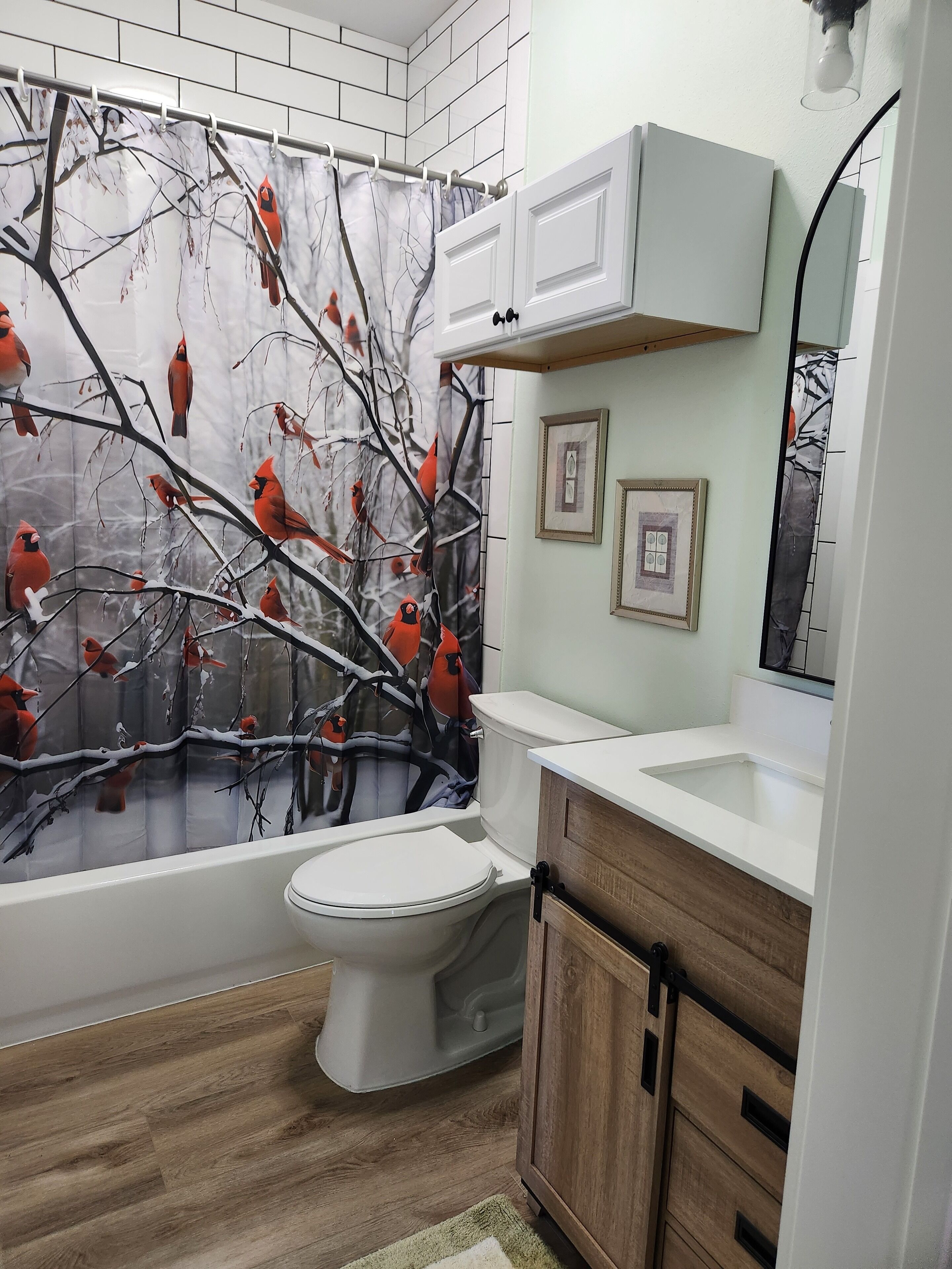 A bathroom with a modern design, featuring a toilet, a vanity with a mirror, and a shower curtain with a tree branch and bird design.