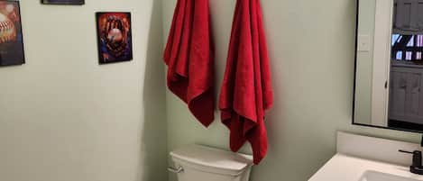 Ein Badezimmer mit Toilette, Waschbecken und zwei roten Handtüchern, die an einem Handtuchhalter hängen.