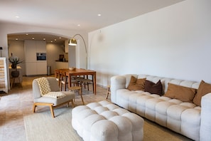 A modern living room with a sofa, ottoman, and dining area.