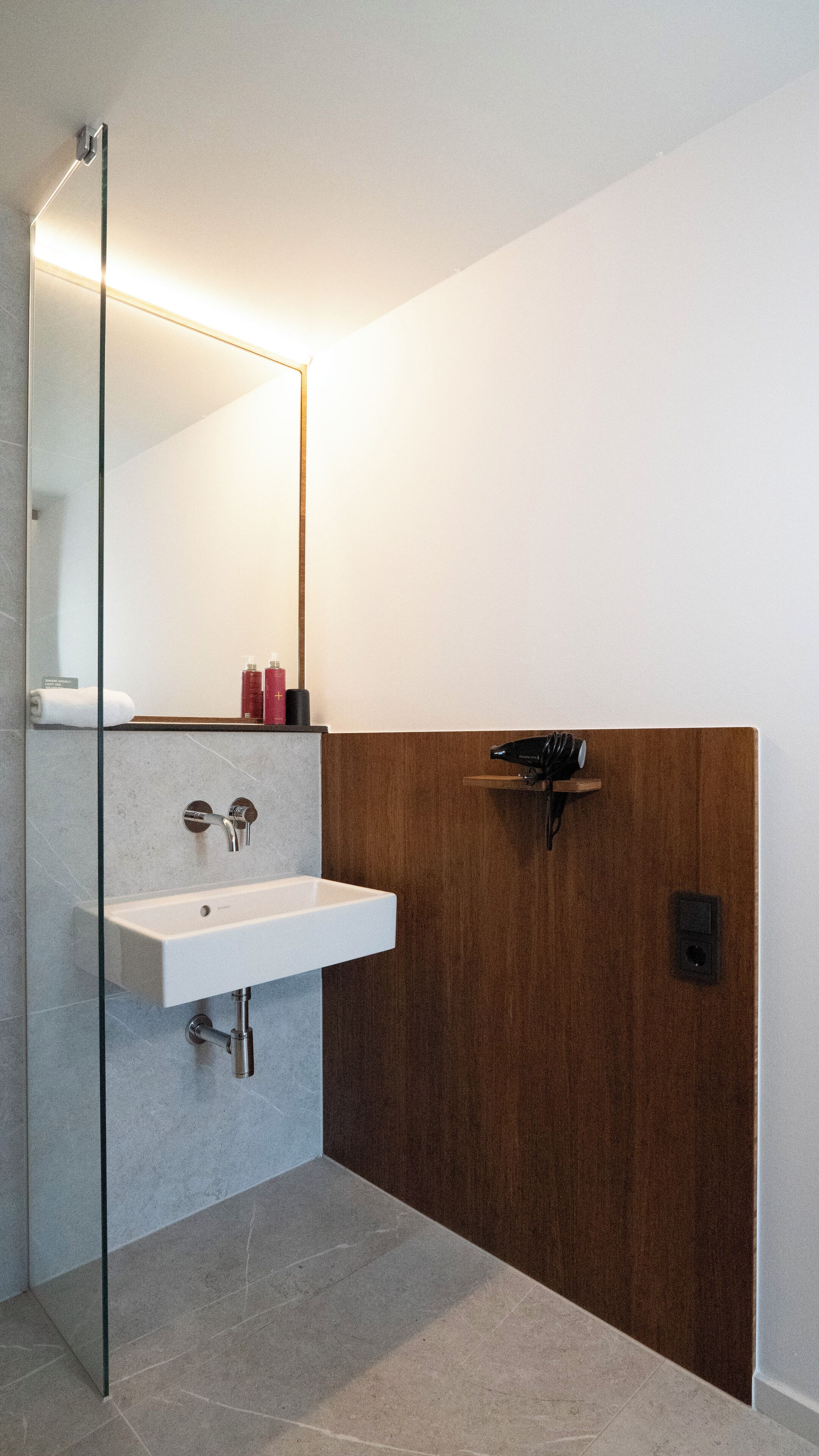 A modern bathroom with a glass shower enclosure, a white sink, and a wooden vanity.