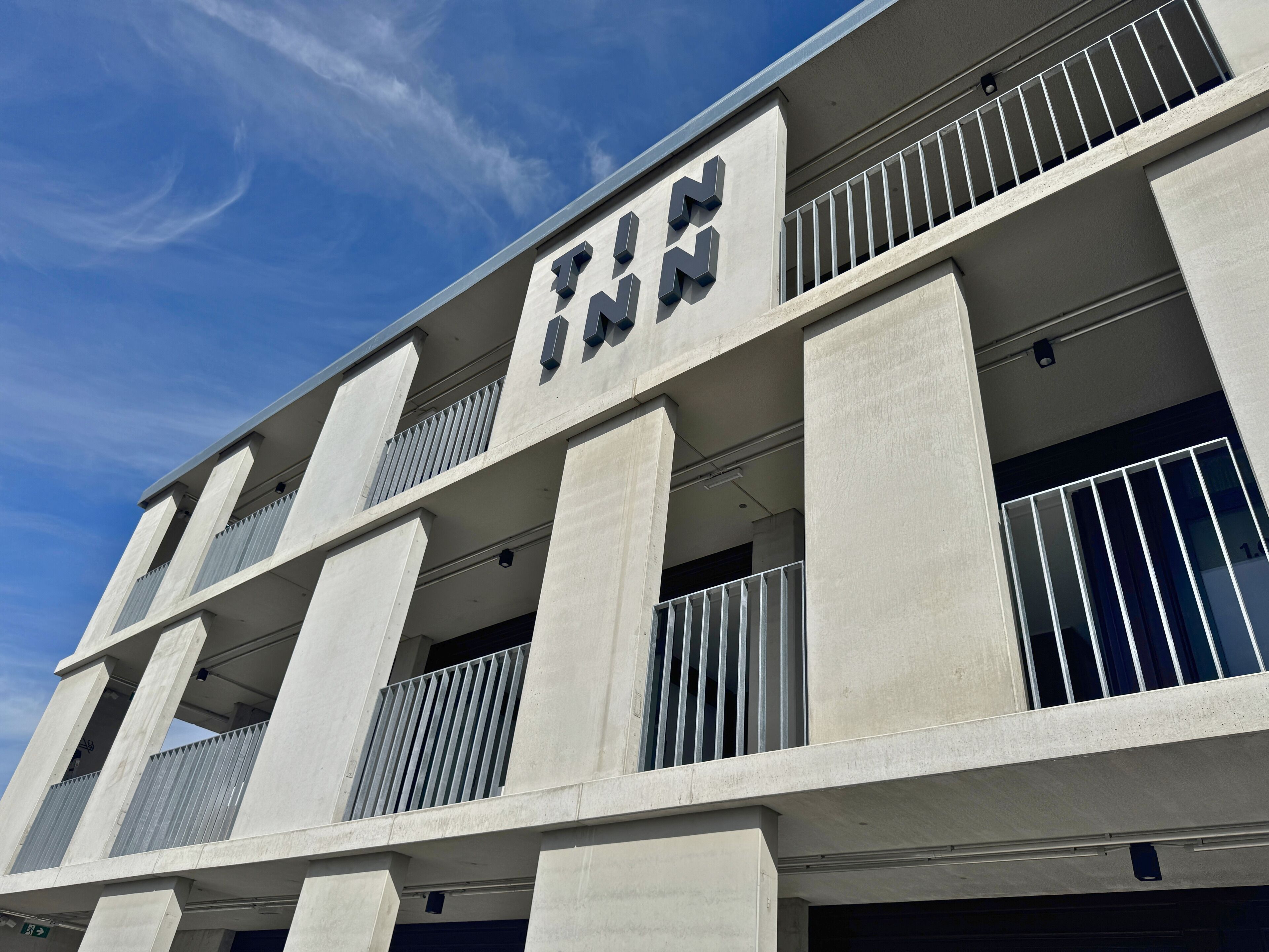 Un edificio moderno con un segno ben visibile 'TWN', caratterizzato da una struttura a più piani con balconi e inferriate.