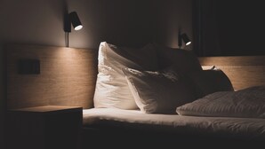 A dimly lit bedroom with a wooden headboard, a bedside table, and two wall-mounted lamps. - TIN INN Nettetal-Kaldenkirchen (Nettetal)
