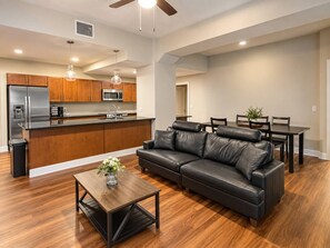 A modern kitchen with a central island, a dining area with a black leather couch, and a wooden coffee table with a vase.