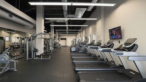Ein Fitnessstudio mit Laufbändern, Kraftgeräten und einem Fernseher an der Wand.