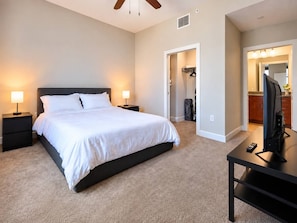 A bedroom with a bed, bedside tables, a desk with a TV, and a walk-in closet.