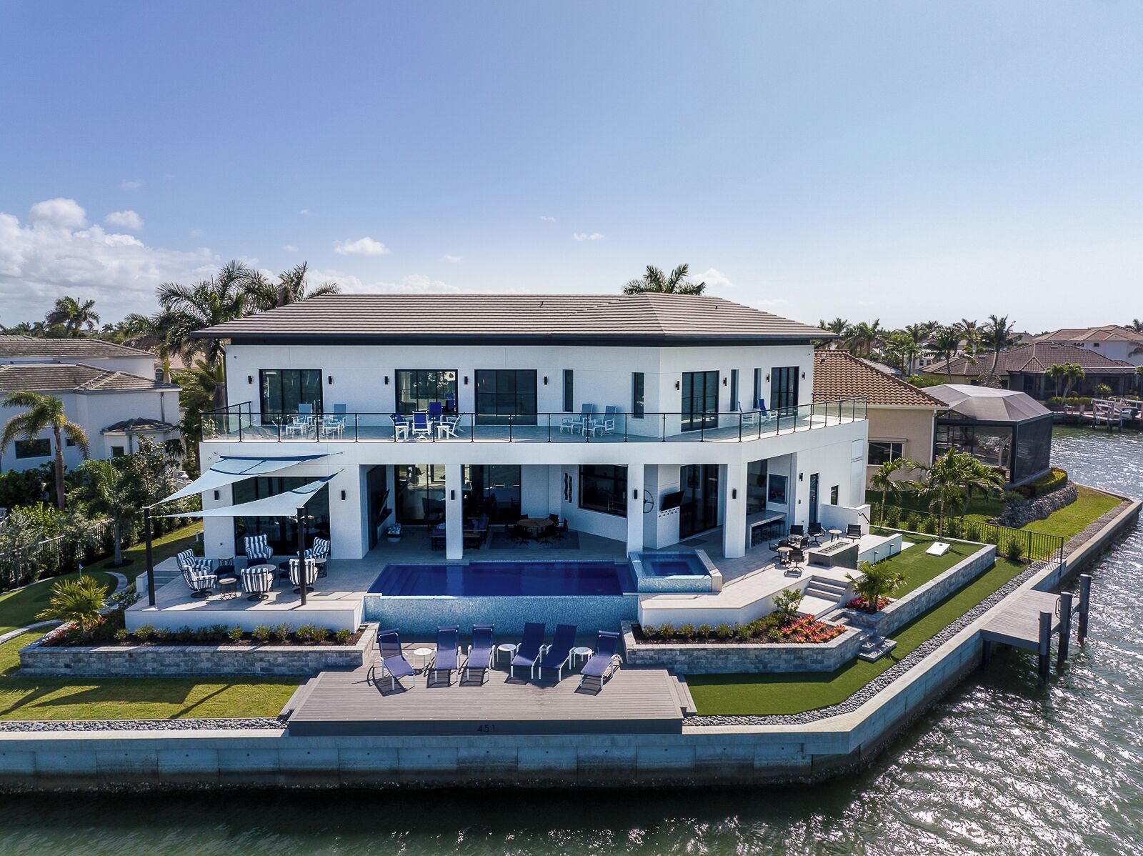 A modern two-story house with a large balcony, a swimming pool, and a waterfront view.