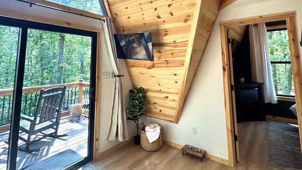Une pièce spacieuse avec un plafond en pente, de grandes fenêtres, une terrasse en bois et un coin salon confortable.