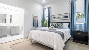 A bedroom with a bed, bedside table, and a window with curtains. - Contemporary 3BR Home by New Orleans Culture (New Orleans)