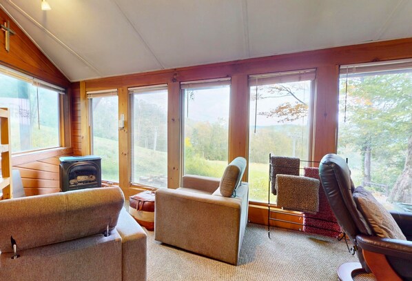 A cozy cabin interior with wooden walls, a fireplace, and large windows offering a view of the outdoors. - Slopesider 14B • Roundhouse • Steps to Slopes (Sugar Mountain)