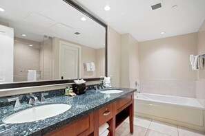A hotel bathroom with two sinks, a large mirror, a bathtub, and a towel rack.