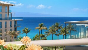 A hotel with a view of the ocean, palm trees, and a balcony with flowers.