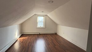 Un ático vacío con suelo de madera, techo inclinado y una pequeña ventana.