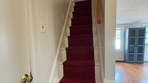 Una escalera con alfombra roja, paredes blancas y barandilla de madera.