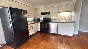 Una cocina compacta con un refrigerador negro, un microondas, un lavavajillas y una estufa.