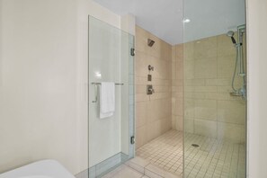 A modern bathroom with a glass shower enclosure, a white bathtub, and beige tiled walls.