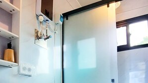 Une salle de bain moderne équipée de toilettes, d’un lavabo et d’une douche. On y trouve des étagères avec des articles de toilette et un porte-serviettes.