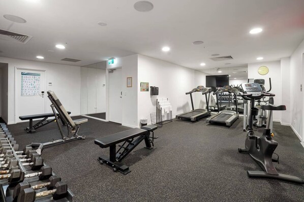 Un gimnasio con cintas de correr, elípticas, bancos de pesas y mancuernas.